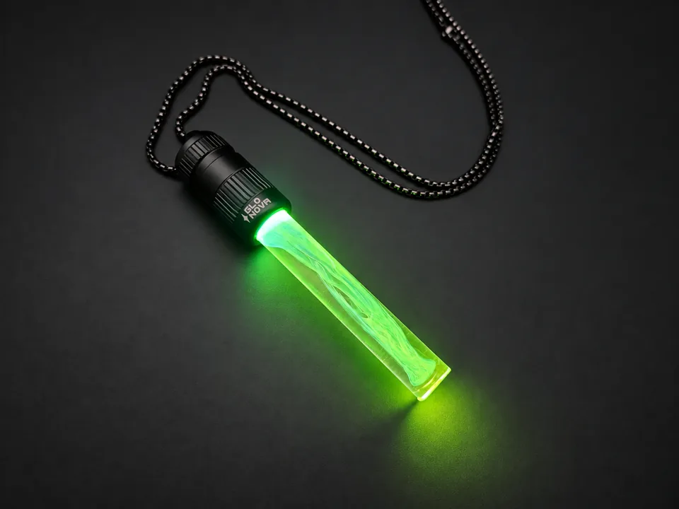 Emerald Dream pendant lying on charcoal with its steel ball chain, green light flowing through the clear rod