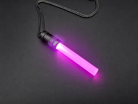 Pink Pulse pendant lying on charcoal with its steel ball chain, pink light filling the clear rod